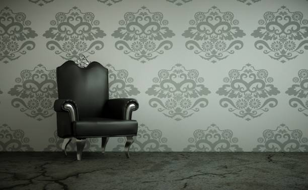 Черное кресло стоит у стены, оклеенной обоями с витиеватым узором.