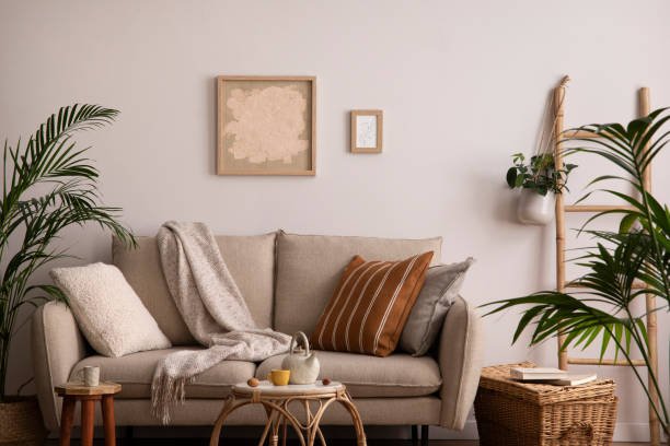 В уютной гостиной есть бежевый диван с подушками и пледами, картины в рамах на стене и зеленые акценты.